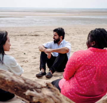 Delwedd o grŵp o dri myfyriwr yn eistedd ar draeth Abertawe.