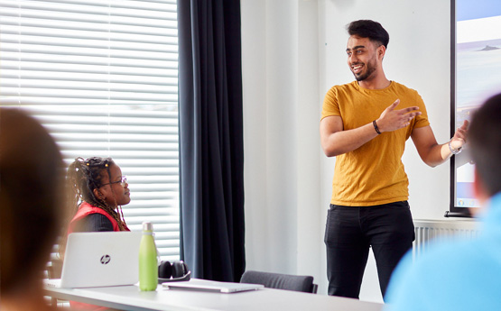 Myfyriwr gwrywaidd yn cyflwyno o flaen bwrdd gwyn