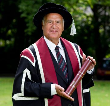 Dyn mewn gwisg graddio yn gwenu wrth y camera