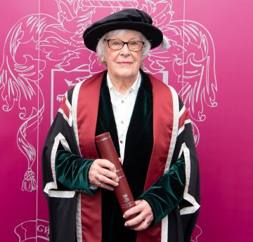 Menyw yn gwisgo gwisg graddio yn edrych at y camera