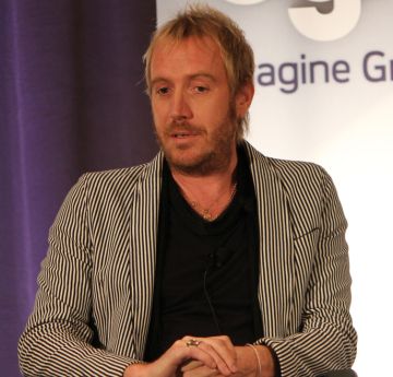 Dyn ar lwyfan yn siarad i'r gynulleidfa