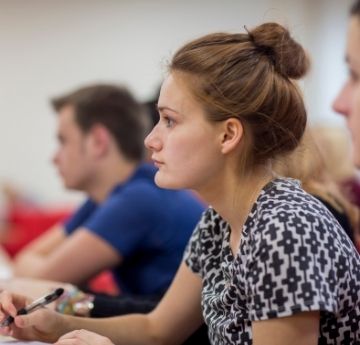 An image of a female student sitting in a lecture with fellow students in background