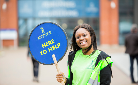 Person yn croesawu ymwelwyr i'r dydd agored. 