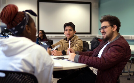 Myfyrwyr yn eistedd o gwmpas desg ac yn trafod