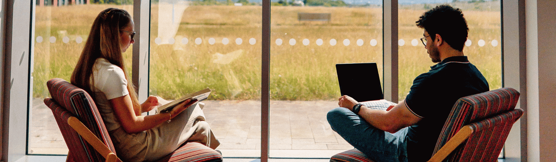 Two students at the Bay Campus Library with a book in hand.