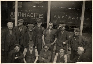 Photograph of Ammanford colliers and workmen standing in a group in front of coal trucks, c1900