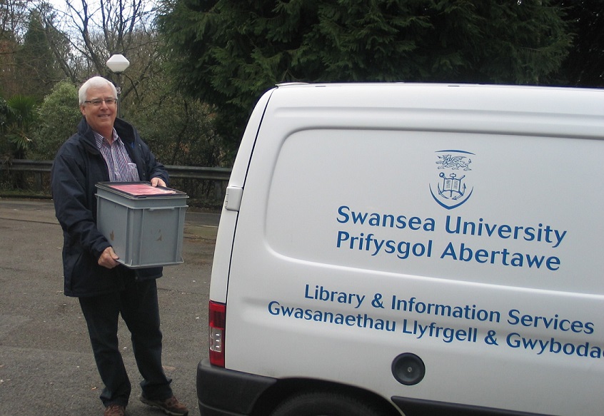 A man holding a box of books next to a Swansea University branded van.