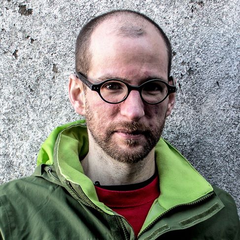 Dr Alan Kellermann mewn siaced werdd o flaen wal lwyd.