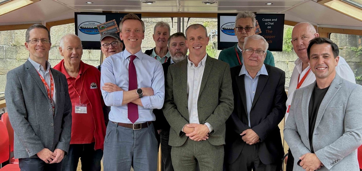 Grŵp o 11 o ddynion yn sefyll y tu mewn i gwch