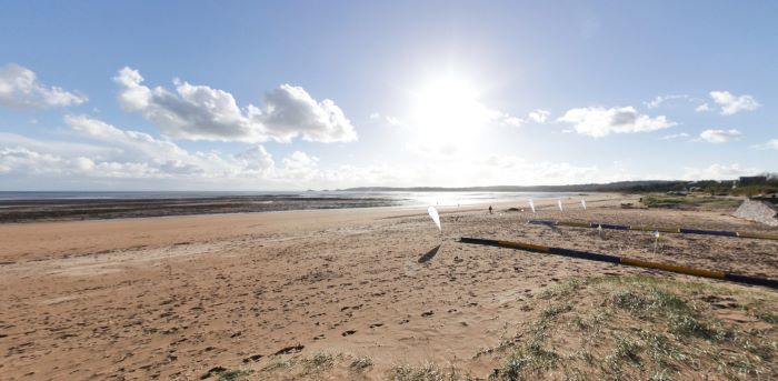 Traeth tywodlyd llydan gyda môr tawel, twyni tywod, ac awyr lachar yng ngolau'r 