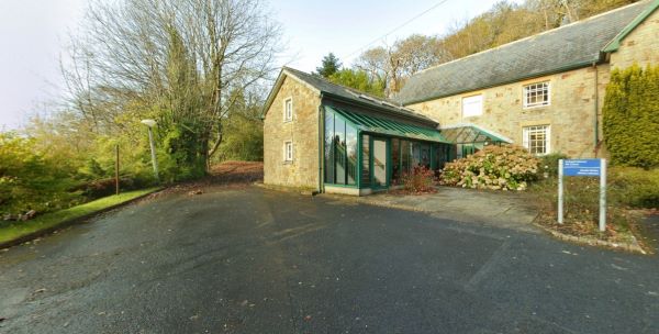 Adeilad llyfrgell garreg gyda mynedfa wydr wedi'i lleoli ymhlith coed a thiroedd
