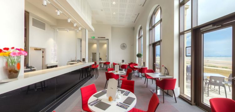 Caffi a bwyty'r Great Hall gyda byrddau, seddi cochion a golygfeydd o'r môr
