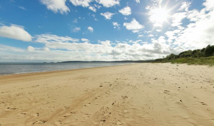 Traeth tywodlyd llydan gyda môr tawel, awyr las, cymylau gwasgaredig, twyni