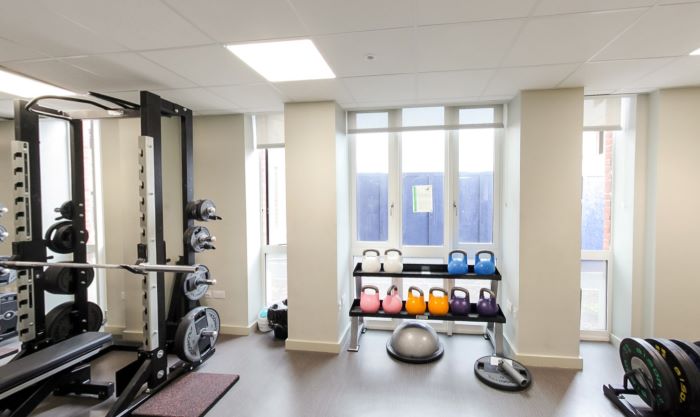 Campfa gyda phwysau, kettlebells, a dau berson yn defnyddio offer cryfder.