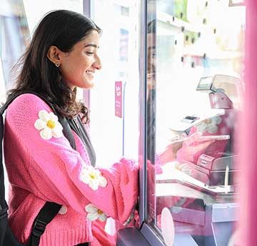 Swansea University Student wearing bright flowery pink cardigan using the ticket machine on a bus