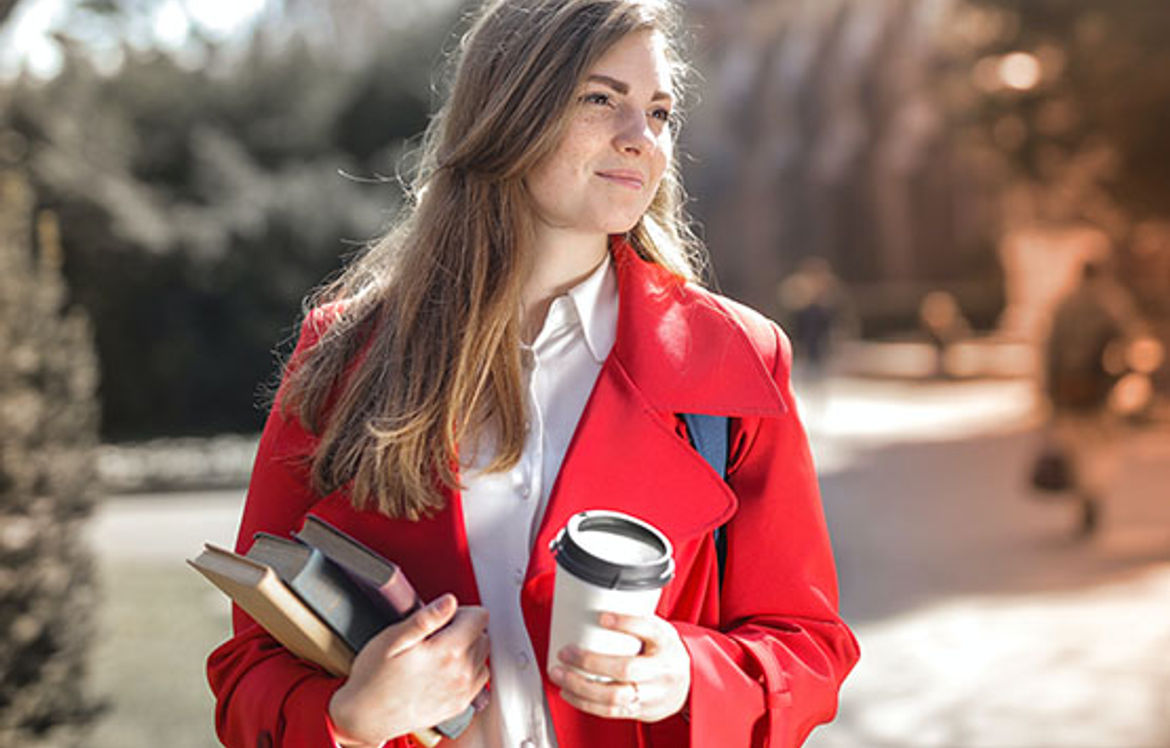A student smiling and having a coffee on campus