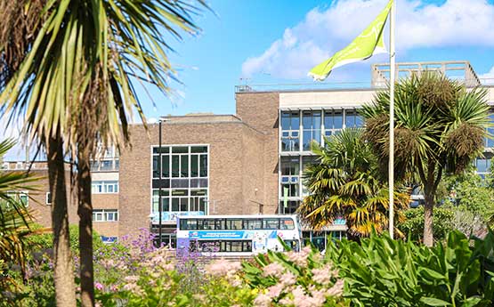 The Green Flag flying on the approach to Fulton House on Swansea University's Singleton Park Campus. Beautiful trees and boarders are in the foreground.
