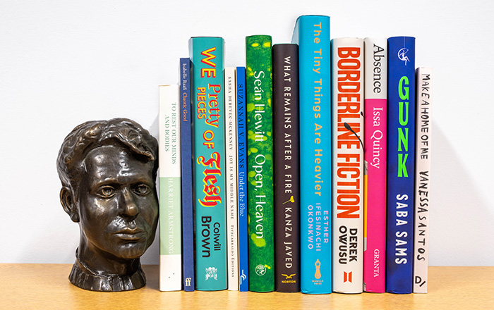 Bookshelf image of the 12 book spines accompanied by bronze bust of Dylan Thomas