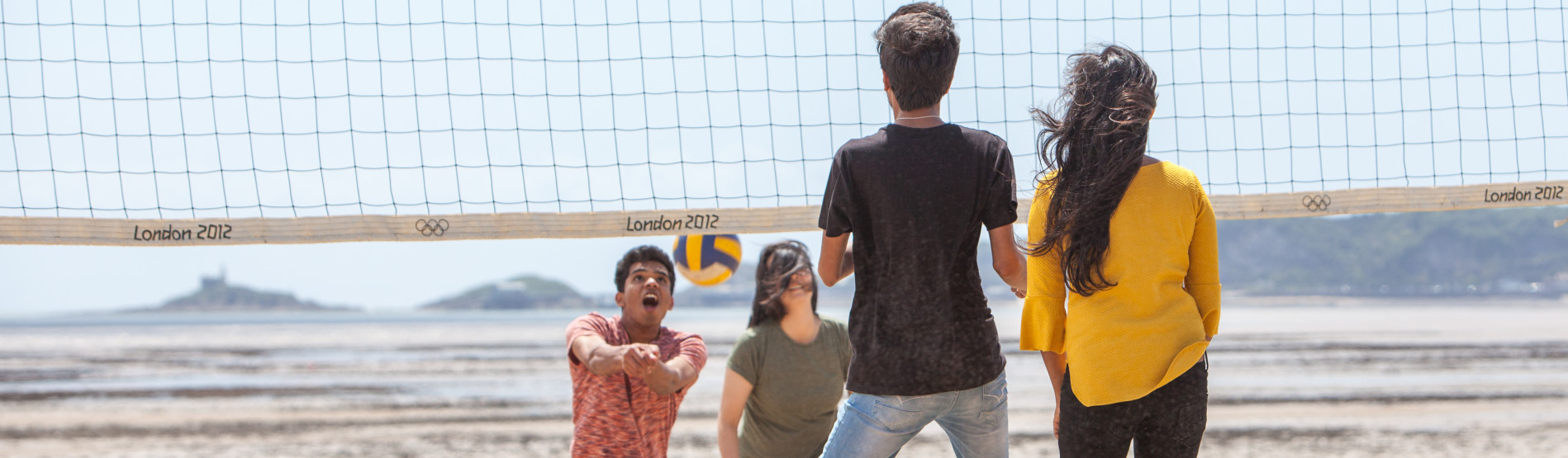Students playing volleyball on the beach in front of campus