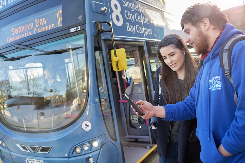 Two students standing next to the number 8 bus looking at their phone