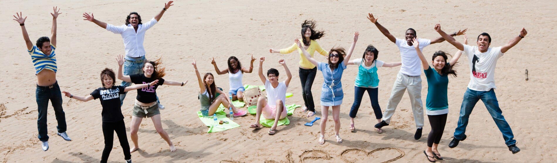 Group of students on Swansea beach with 'we heart swansea' carved into the sand.