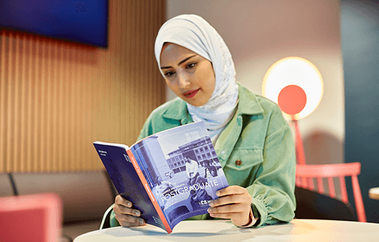 A female student reading Swansea University Postgraduate study prospectus