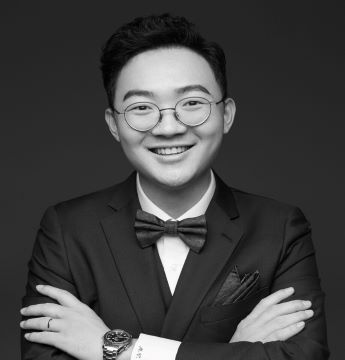 A portrait of Vincent Zhang, dressed in a formal, dark suit , who smiles to the camera.