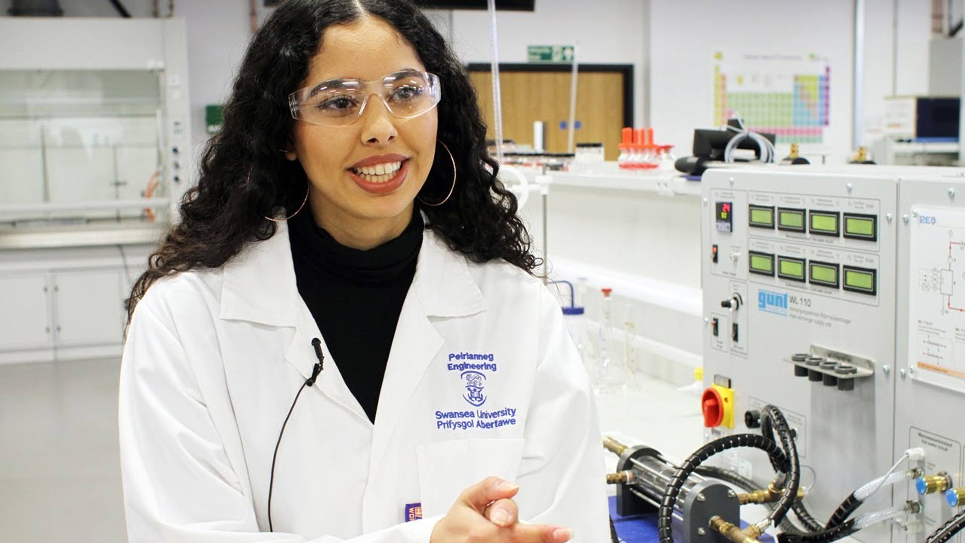 Female student from Egypt in a laboratory coat talking in a science lab. 