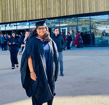 A photo of Rashmi in her graduation gown and cap in front of Swansea Arena on her graduation day.