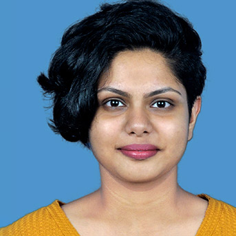 Female Indian student looking at the camera wit a blue background and orange top.