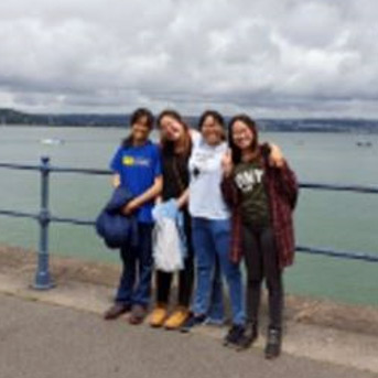 A group of four students standing by a fence next to the sea.