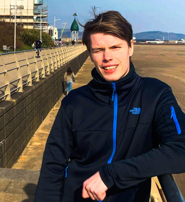 Male Norwegian student on Swansea beach, smiling but squinting from the sunshine