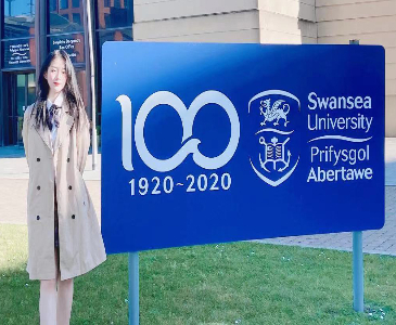 student standing next to swansea university sign on bay campus