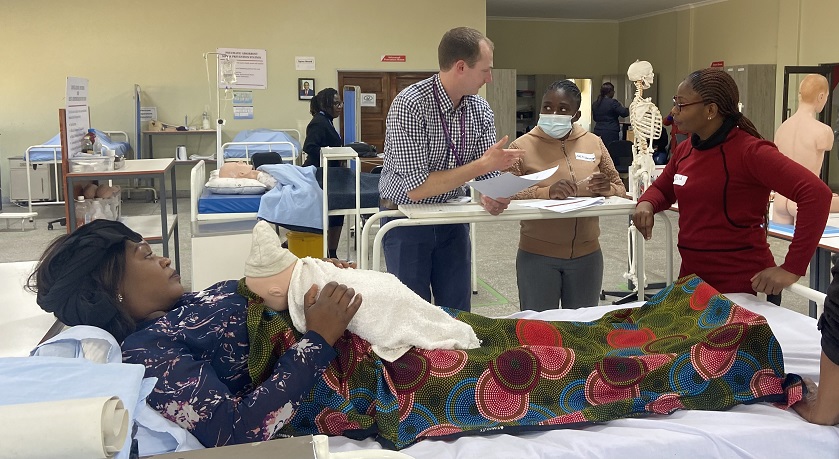 Students and lecturer around a hospital bed containing a simulated patient and mannequin baby