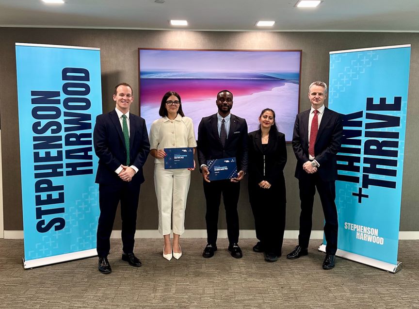 Five people standing in front of Stephenson Harwood banners.