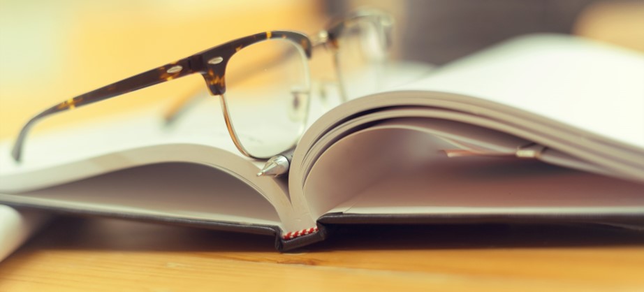 Book open in the middle with spine and pages showing. There are reading glasses on top of the book.