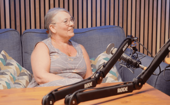 A woman sitting on a grey sofa speaking into a microphone for a podcast.
