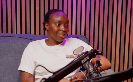 A woman sitting on a grey sofa speaking into a microphone for a podcast.