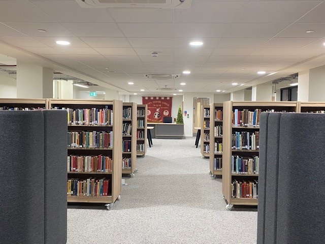 Rows of book shelving leading towards the Information Desk at the South Wales Miners' Library. There is a red banner above the desk.