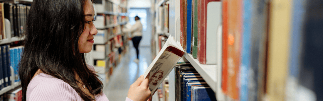 A student selecting a book from a library shelf