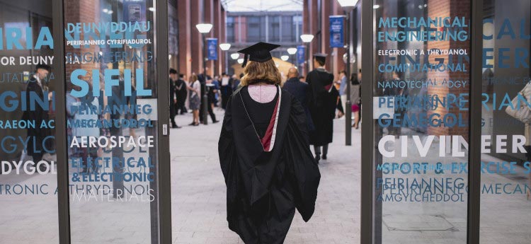 Student walking through engineering building in graduation gown. 