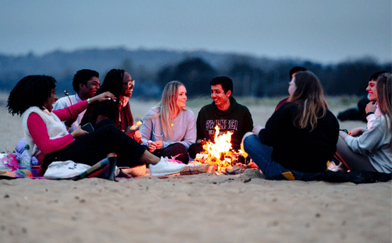 Students chatting around a camp fire on Swansea beach at night