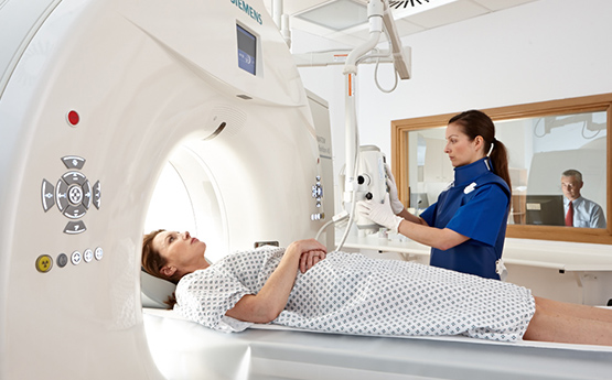Woman in MRI scanner with Clinical Support staff operating MRI in background 