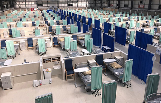 rows of hospital bed and screens laid out in a temporary field hospital location