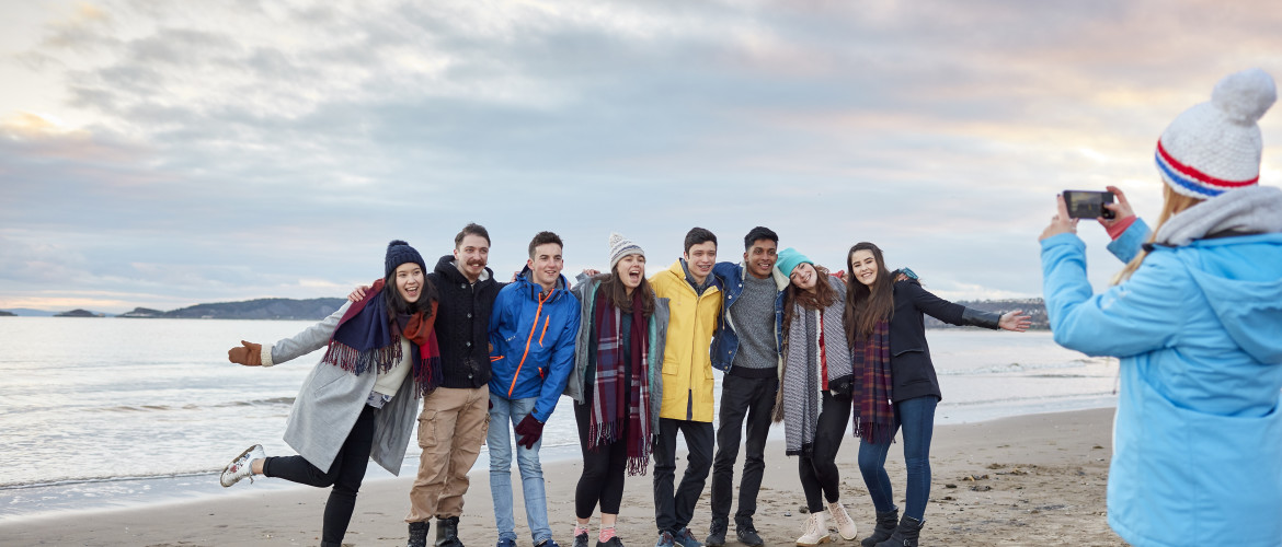 Group of males and females on beach in winter, having their photo taken