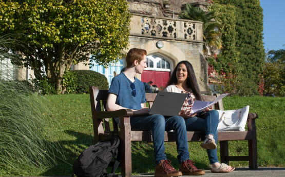 Two students sitting on a bench studying, outside the Singleton Abbey building.