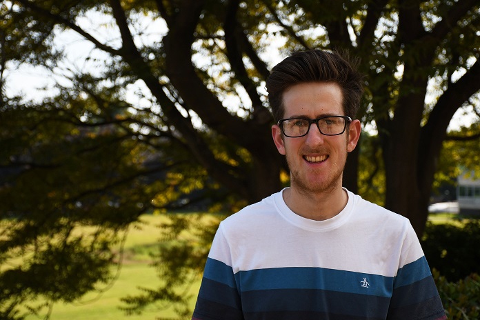 Student wearing glasses standing in park and smiling at the camera