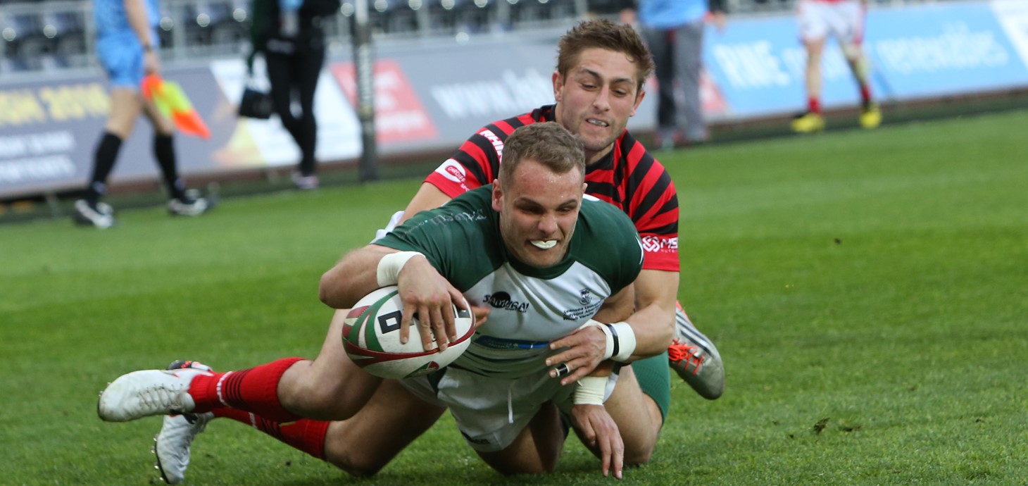 A Swansea rugby player getting tackled by a Cardiff player as he scores a try. 