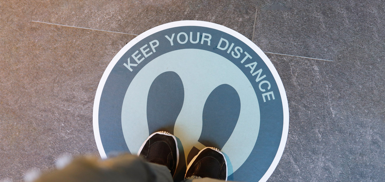 A man's feet standing on a floor sign that says 'Keep your distance' 