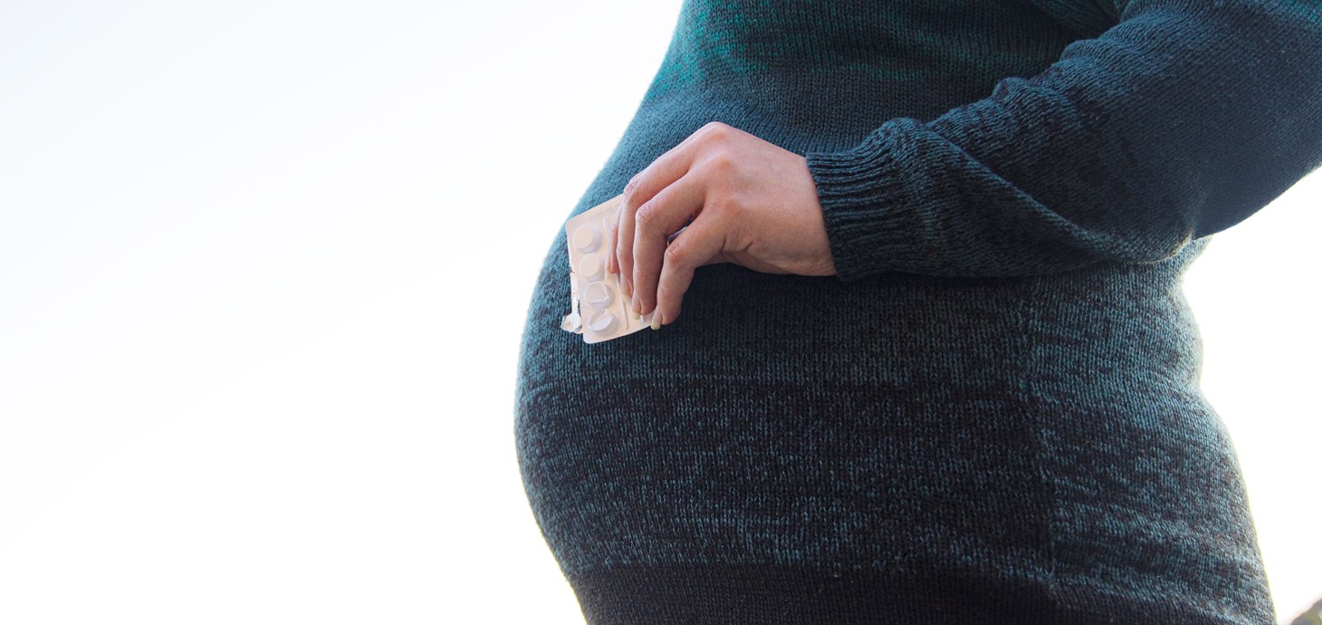 Image shows pregnant woman holding asthma medication.